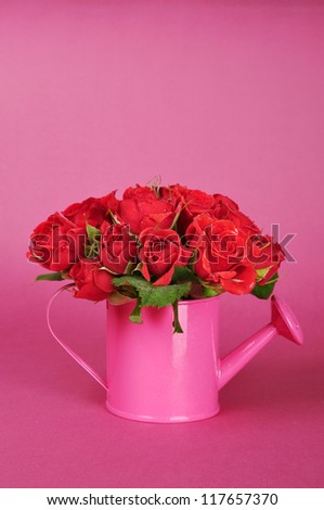 bouquet of red roses in a pink watering can on a pink background