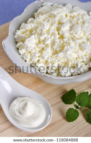 Cottage cheese in bowl with sour cream on wooden cutting board