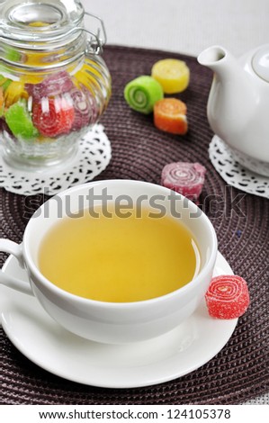 Tea in cup, sweet jelly candies in glass jar and teapot