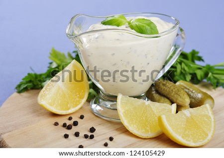Tartare Sauce  in a  gravy boat with cucumber and lemon on wooden cutting board