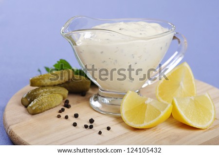 Tartare Sauce  in a  gravy boat with cucumber and lemon on wooden cutting board