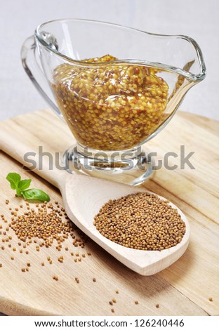 Mustard sauce in a gravy boat and mustard seeds in a wooden spoon