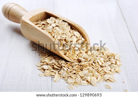 Oat flakes in wooden scoop on white wooden background