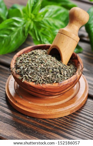 Dry basil in wooden bowl and fresh basil on wooden background