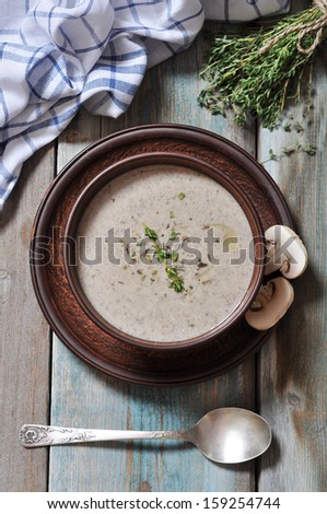 Mushroom cream soup with herbs in brown bowl over wooden background