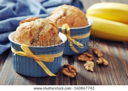 Banana muffins in baking mold with nuts over wooden background