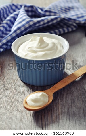Greek yogurt in a ceramic bowl with spoons on wooden background