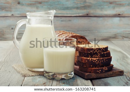 Jug of milk, glass and sliced bread on wooden background