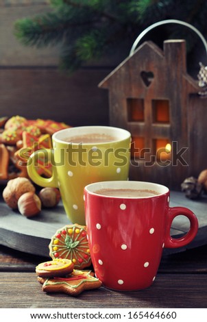Two cups of hot chocolate, a fir tree branch and ginger biscuits on a wooden background