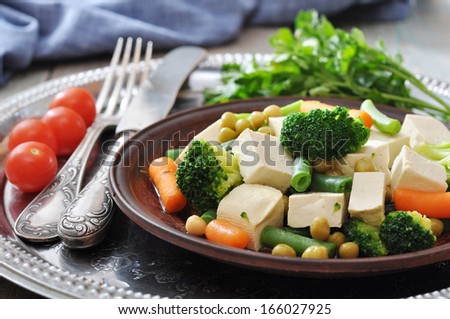 Tofu with boiled vegetables on plate and tomato closeup