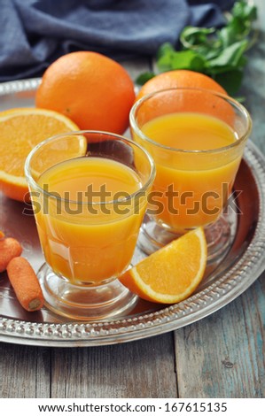Orange and carrot juice in glass with mint,  fresh vegetables and fruits on round tray