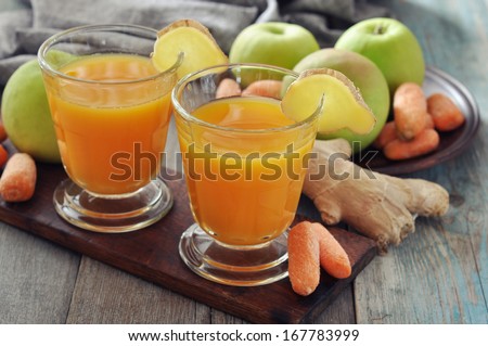 Apple and carrot juice in glass with ginger,  fresh vegetables and fruits on wooden background