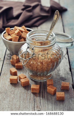 Brown candy sugar in glass jar on wooden background