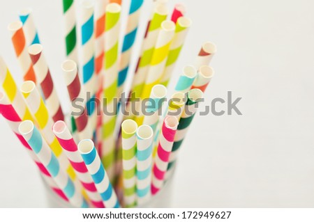 Striped drink straws of different colors in glass on light background. Selective focus.