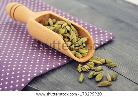 Dry cardamom seeds in scoop closeup on wooden background