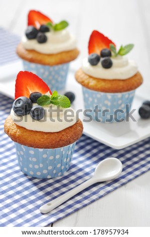 Cupcakes decorated with butter cream and fresh berries in polka dot cases on wooden background