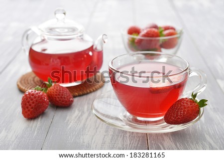 Strawberry tea in glass cup with teapot and fresh berries on wooden background