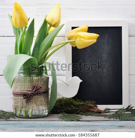 Beautiful tulips bouquet in vase with blank blackboard and chalk on wooden background