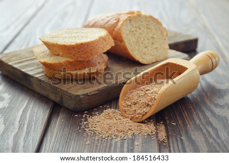 Wheat bran in bowl with sliced bread on wooden background