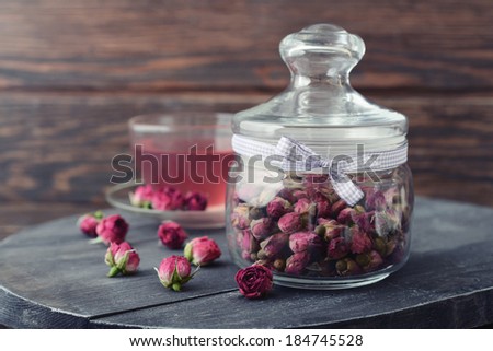 Tea rose flowers  in glass jar and tea on wooden background