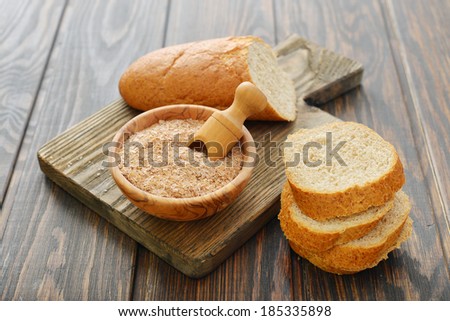 Wheat bran in bowl with sliced bread on wooden background