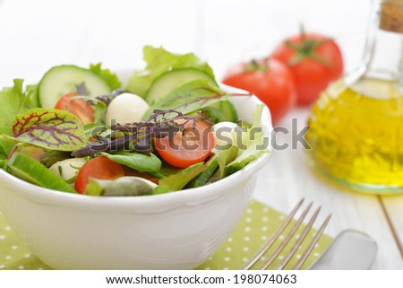 Salad mix with different kinds of salad leaves, tomato and mozzarella cheese in bowl on wooden background