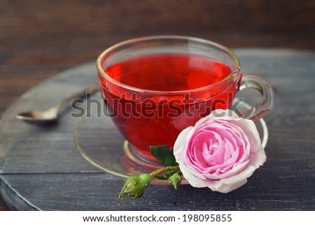 Tea rose flowers and cup of tea on wooden background