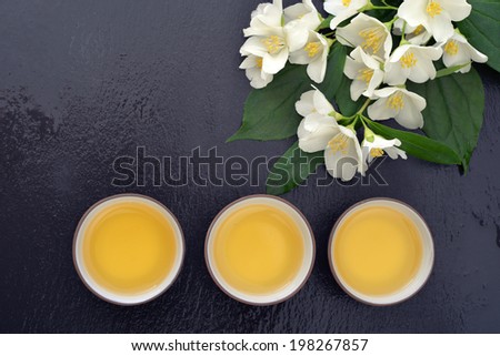 Green tea in cups with jasmine flowers on wet  graphite background