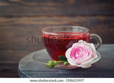 Tea rose flowers and cup of tea on wooden background