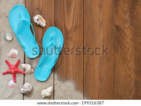 Blue Flip-flops with red starfish and sand on wooden background with copy space, top view.