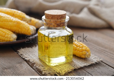 Corn oil in bottle with corn cobs on wooden background