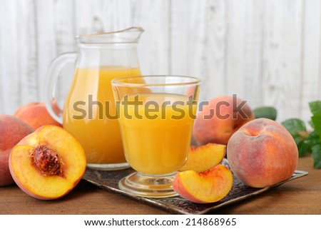 Peach juice in jug and glass with fresh peaches on wooden background