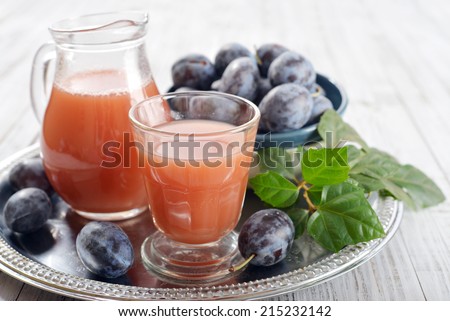 Plum juice in jug and glass with fresh plums on wooden background