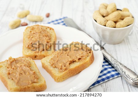 Peanut butter sandwich on plate with nuts on wooden background