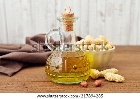 Peanut oil with raw peanuts on wooden background