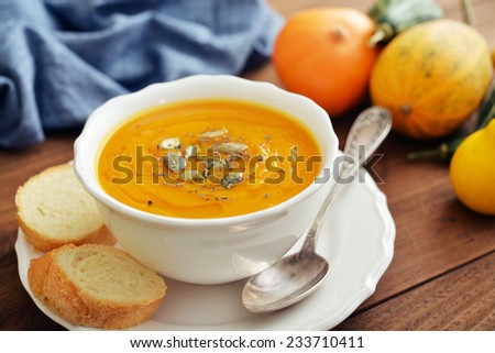 Bowl of pumpkin soup with decorative pumpkin on wooden background