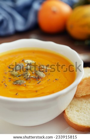 Bowl of pumpkin soup with decorative pumpkin on wooden background