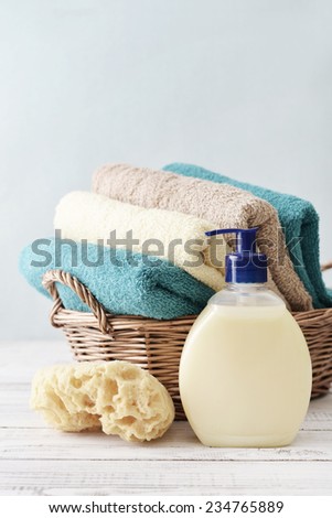 Liquid soap, sponge and towels in a wicker basket on a light background