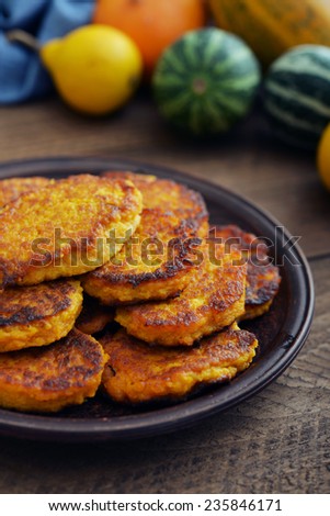 Pumpkin pancakes on plate with decorative pumpkin on wooden background