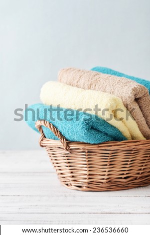 Bath towels of different colors in wicker basket on light background