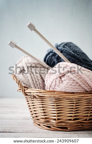 Wool yarn in coils with knitting needles in wicker basket on light blue background