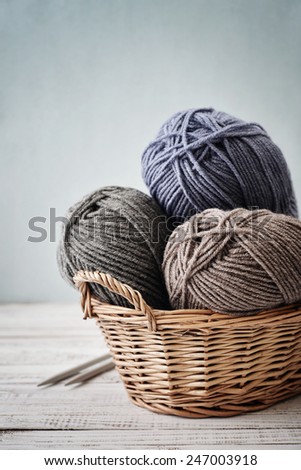 Wool yarn in coils with knitting needles in wicker basket on light blue background