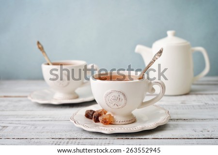Cup of tea and sugar with teapot over blue background