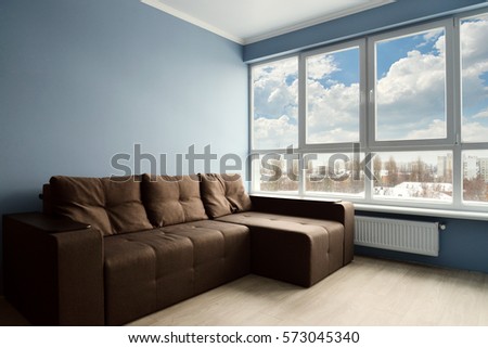 Clean family room with brown couch and large windows showing bright winter landscape in background.