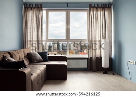Clean family room with brown couch and large windows showing bright spring landscape in background.