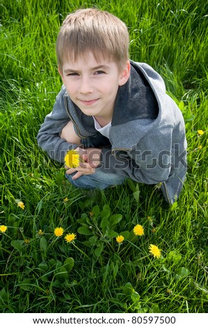 eight years old boy sitting on grass with dandelion in his hand