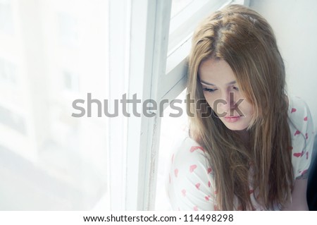 Beautiful sad girl misses the window