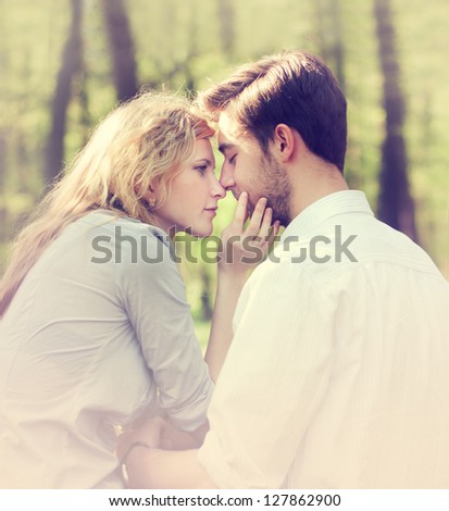 young couple kissing while sitting in a summer forest
