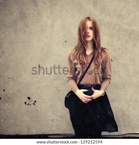 beautiful young girl with a camera on the background wall. girl is dressed in the style of hipster