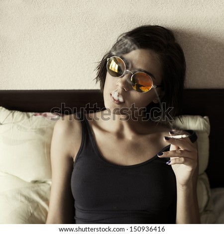 beautiful girl with round glasses hipster smokes in bed